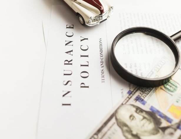 Image of document titled "Insurance Policy" with money, car, and magnifying glass sitting on top of the document.